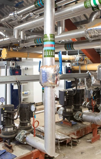 A network of insulated industrial pipes, pumps, and control valves in a large building services training facility A network of insulated industrial pipes, pumps, and control valves in a large building services training facility